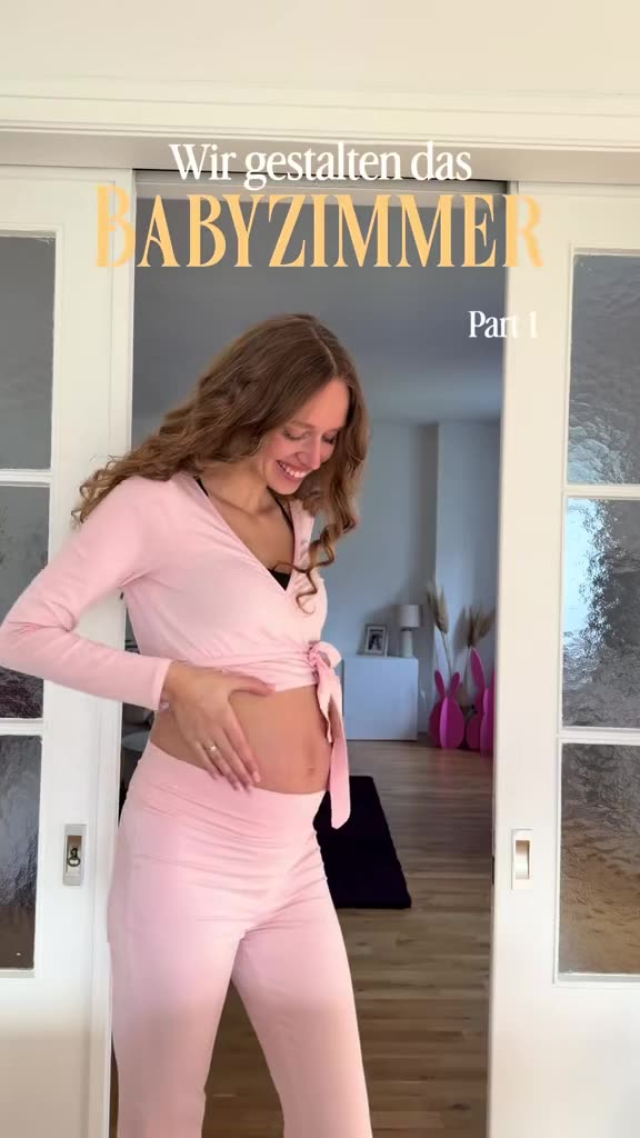 Melina steht schwanger in rosa Kleidung in einer Zimmertür